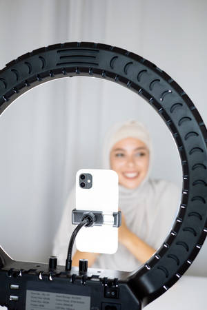Woman in white hijab smiling while taking a selfie with phone on ring light. — Lit iPhone Picture