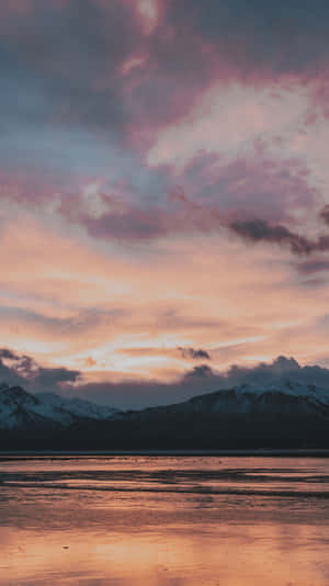 Snow-capped mountains at sunset reflected in a calm lake under pink and orange sky.