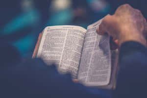 Hand hält offene Bibel mit sichtbarem Text unter blauem Licht — Sunday School Wallpaper