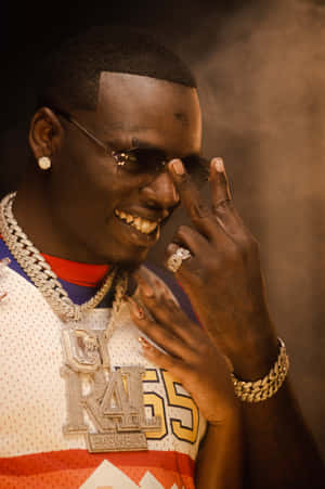 Man in sports jersey and gold chains smiling with smoke in background.