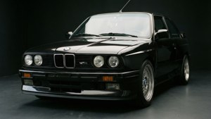 En minimalistisk studio-bakgrunnsvegg av en svart BMW E36 M3 med dramatisk belysning og refleksjoner.