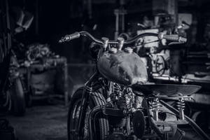 Vintage motorcycle in a cluttered garage with tools and machinery in the background.