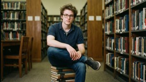 Young man with glasses sitting on books in a library