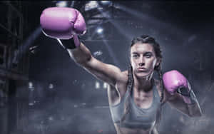 A female boxer in pink gloves raises her fist in a dim lit gym. — Boxing day Wallpaper