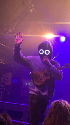 Musiker mit Maske spielt Ukulele auf der Bühne unter bunten Lichtern.