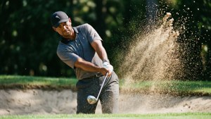 Tiger Woods memukul keluar dari bunker dengan pasir beterbangan.