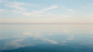 Minimalistisch en rustig uitzicht op de Atlantische Oceaan met glasachtig water en pastelkleurige hemelreflectie.