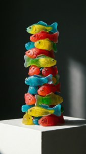 Pila di sculture di pesci di plastica colorati su un piedistallo bianco.