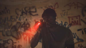 Uomo con berretto che tiene dispositivo rosso acceso contro muro di graffiti di notte. — Candyman Sfondi
