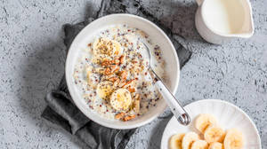 Eine Schüssel Haferflocken mit Bananenscheiben, Walnüssen und Chiasamen mit Milch und zusätzlichen Bananenscheiben in der Nähe.