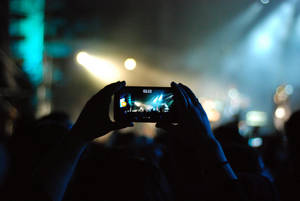 Hands holding phone recording a live concert under colorful stage lights.