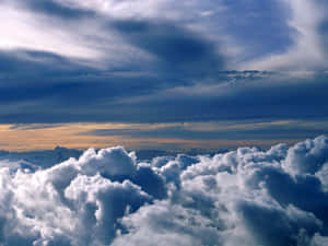View from above fluffy clouds with dark storm clouds and golden sunset horizon.