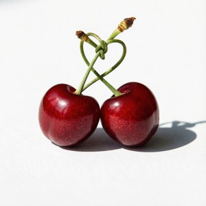 Two cherries with stems tied in a heart shape on white surface — Cherry Wallpaper
