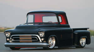 Black classic custom pickup truck with red interior parked on a road near mountains.