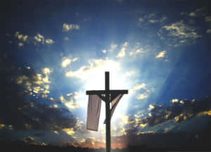 Silhouette of a cross with cloth against a radiant sunset sky with clouds. — Christ Is Risen Picture