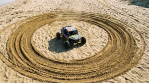 Pemandangan dari atas sebuah mobil buggy pantai yang membuat jejak ban melingkar di pasir, ceria dan penuh warna.