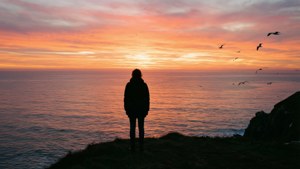 Una silueta de una persona en un acantilado con vista a un océano tranquilo al atardecer.