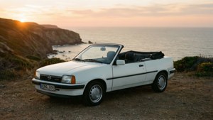 White convertible car parked on cliff overlooking ocean at sunset.
