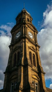 Towering clock tower with ornate stonework under a bright blue sky with clouds. — Palmerston North Picture