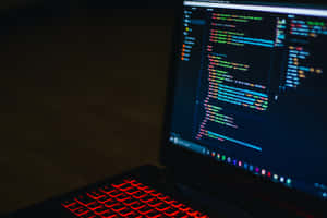 Laptop with red backlit keyboard showing colorful code on screen in dark room — Coding Picture