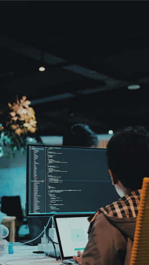 Person coding on computer in dimly lit office at night
