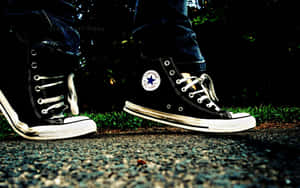 Tênis Converse preto desgastado com cadarços e solas brancas sobre cascalho perto da grama. — Converse Papéis de Parede