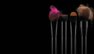 Fire makeup-børster med farvet pudder, der sprænger ud fra deres spidser på en sort baggrund. — Klæd Dig For At Impress Wallpapers