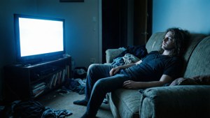 Eine Person liegt apathisch auf einer Couch in einem schwach beleuchteten Raum