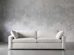 A modern off-white sofa against a textured gray concrete wall in a minimalist room. — Couch Wallpaper
