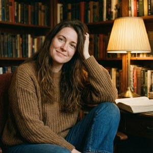 Sara Canning in una biblioteca accogliente con luce calda della lampada, circondata da libri, rilassata e intellettuale.