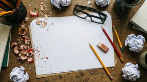 A messy desk with pencil, paper, eraser shavings, and crumpled paper.