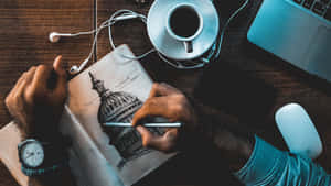 Artista dibujando edificio del Capitolio en cuaderno con café, computadora portátil y auriculares sobre escritorio de madera — Dibujar Fondos de pantalla