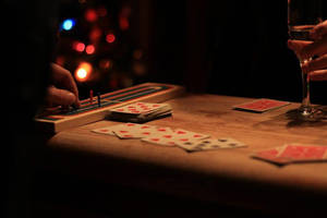 Close-up of hands playing cards and moving game pieces on a wooden table at night. — Cribbage Picture