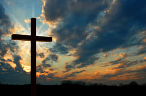 Silhouetted cross against a vibrant sunset sky with sun rays and clouds. — Cross Wallpaper