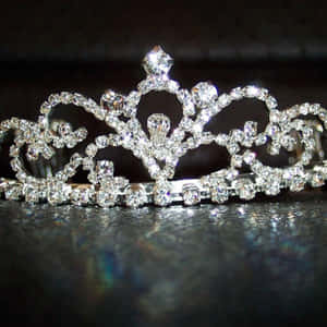 A glittering diamond tiara resting on a dark reflective surface. — Crown Wallpaper