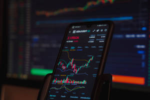 Smartphone showing crypto trading chart with computer monitor in background
