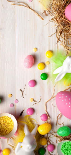 Easter eggs and bunny decorations on a wooden table with hay and sprinkles.