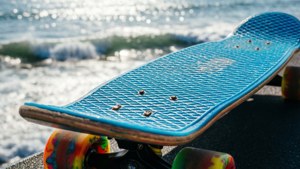 Lähikuva surfskate-laudasta, jossa on värikkäät pyörät ja taustalla kimalteleva meri.