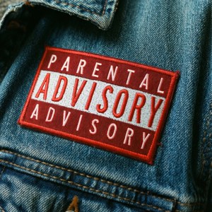 Product shot of a red Parental Advisory patch sewn onto a denim jacket with natural lighting.