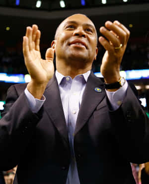 Man in suit clapping at sports event with crowd in background.