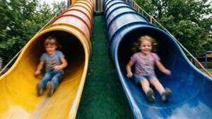 Due bambini che scivolano in gara su uno scivolo doppio, angolo dinamico e movimento sfocato.