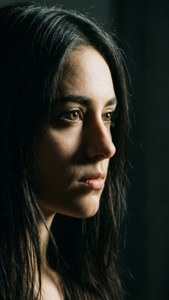 En filmisk nærbillede profil af en ung kvinde med langt sort hår under dramatisk belysning.