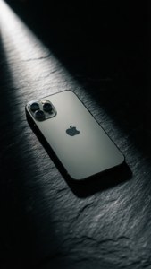 An iPhone lit by a single spotlight on dark slate, dramatic contrast