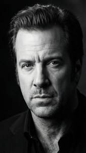 Potret hitam putih David Spade dengan pencahayaan dramatis.