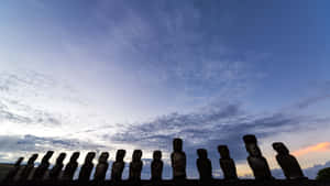 Row of ancient moai statues silhouetted against a twilight sky with orange and blue clouds. — Anime Easter Wallpaper