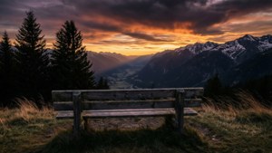 Un banc solitaire face à une vallée montagneuse au coucher du soleil, avec des cieux dramatiques et une ambiance de souvenir silencieux.