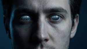 Biografisk tapet af en ansigtsløs person med glasagtige øjne, der reflekterer en dyster byscene i kolde blå toner.