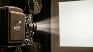 Proyektor film lama dengan MUBI terukir di sisi, debu di berkas cahaya