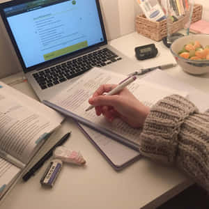 Mano che scrive appunti su una scrivania da studio con laptop e ciotola di frutta. — Study Aesthetic Sfondi