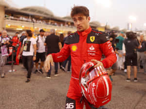 Ferrari driver Charles Leclerc holding his helmet at a race track during sunset.